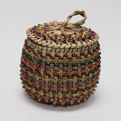 Colour photograph of an ash basket decorated with several colors. The handle of the lid is made of sweetgrass.