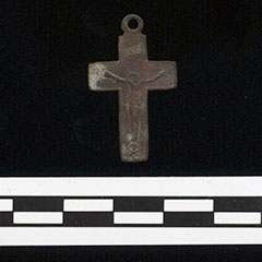 Photographie couleur d'un pendentif en croix fait d'alliage cuivreux sur lequel on retrouve l'illustration du Christ.