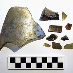 Photographie couleur de dix morceaux de bouteille de verre. Tous ont une taille et une forme différentes. Le code Borden peut être lu sur un morceau.