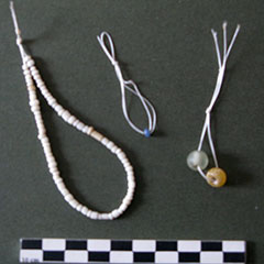 Colour photograph of three sets of beads strung on threads. Little white beads are placed to the left, a blue bead is placed in the center and two bigger beads are placed to the right.