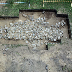 Photographie couleur de plusieurs pierres équarries, vues de haut, formant la fondation d'une habitation. Des ficelles, placées à la verticale et à l'horizontale forment des carrés au niveau du sol.