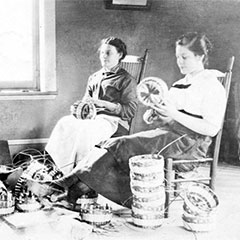 Photographie en noir et blanc de trois abénakises, assises près d'une fenêtre, qui confectionnent des paniers.