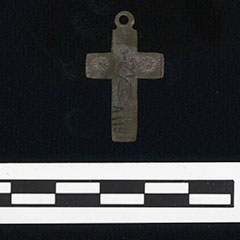 Colour photograph of a cross-shaped pendant made of copper alloy.