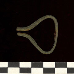 Photographie couleur d'un petit instrument fait d'alliages cuivreux qui possède une structure arrondie à droite et rapprochée à gauche.