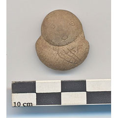 Colour photograph of a beige clay concretion forming two round shapes onto which a face and hands are engraved.