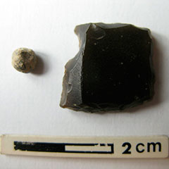 Colour photograph of a lead bullet and of a gunflint made of black flint.