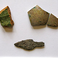 Colour photograph of a shard of glass, a piece of terracotta and an iron arrowhead.