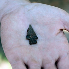 Close-up colour photograph of a hand holding an iron arrowhead.