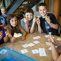 Colour photograph of children around a table, holding cards and artifacts in their hands.