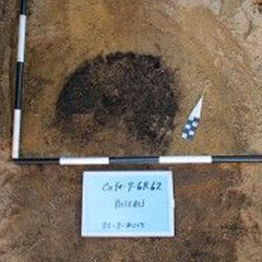 Colour photograph of a circle of ashes and a placard that says: Pieu.