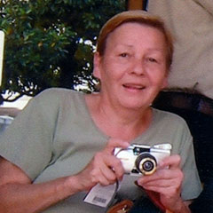 Colour photograph of a smiling woman wearing a green t-shirt. She is holding a camera in her hands.